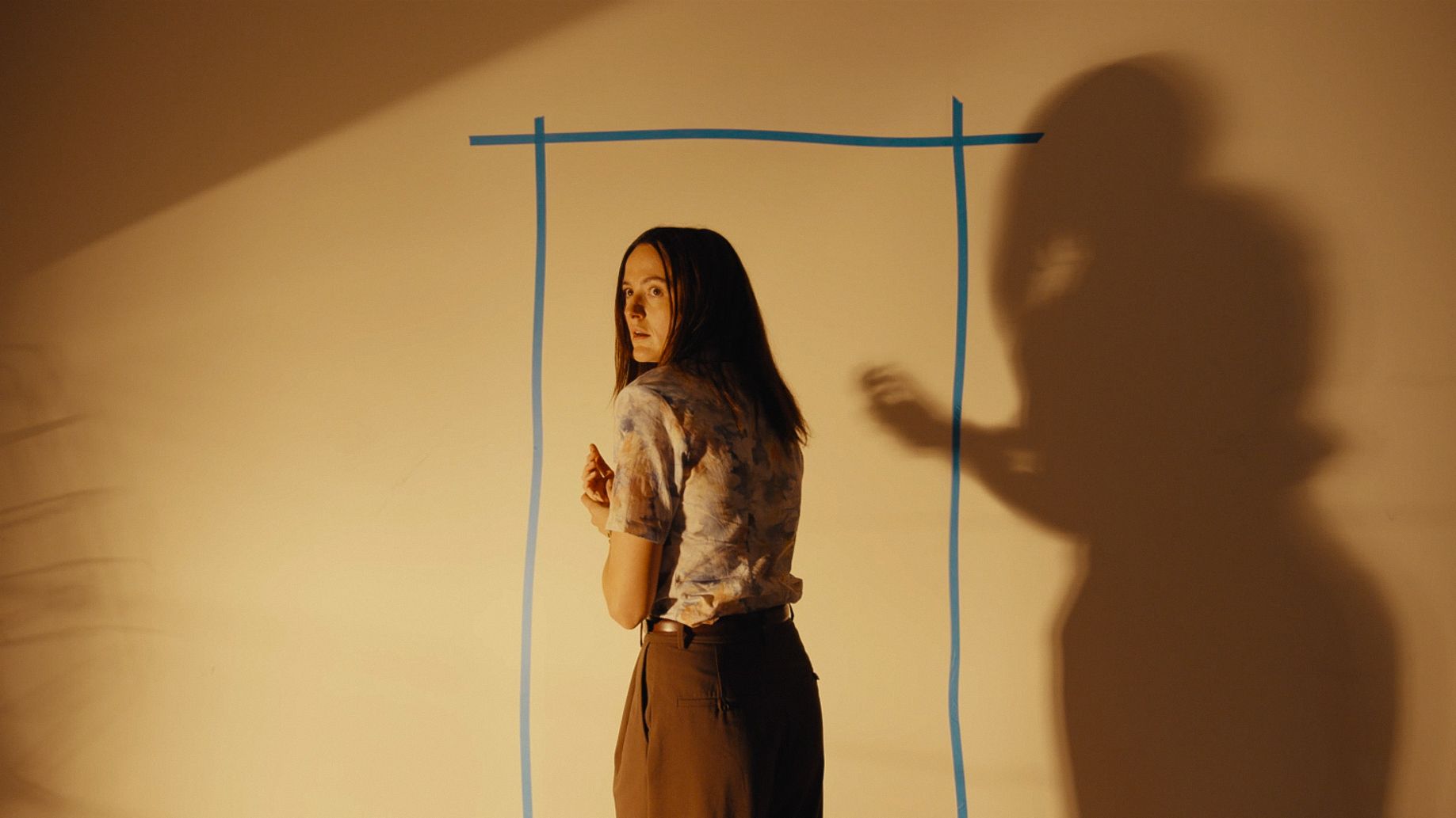 Renate Reinsve in front of a yellow wall with blue tape showing a door's outline