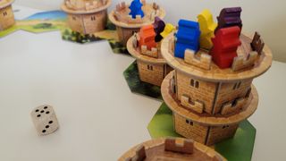 A half-circle of cardboard towers from Wandering Towers on a plain surface, with meeples and a die also in view