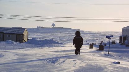 A person walking through snow toward an air defence radar station in Cambridge Bay, Nunavut.