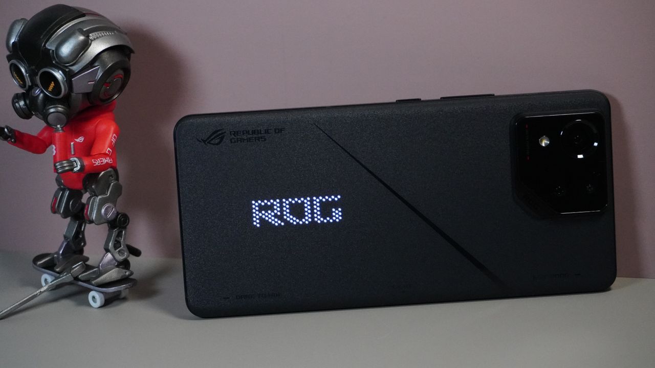 The Asus ROG Phone 8 on a grey and pink background, sat alongside some ROG merchandise