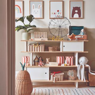 Wooden shelving unit with books, cuddly toys and ornaments underneath four animated prints on wall
