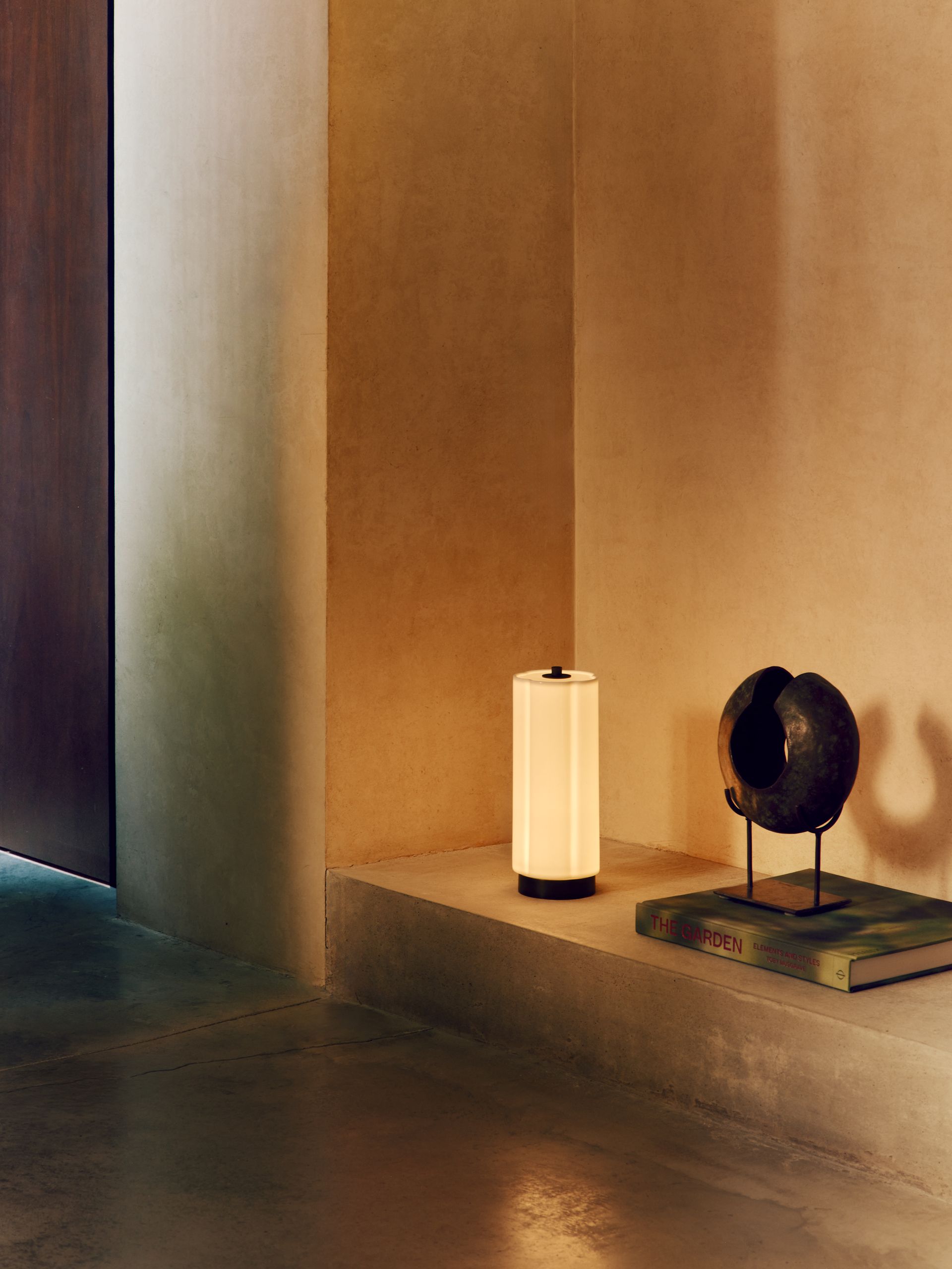 A glass portable lamp on a low shelf in a modern, minimalist entryway.