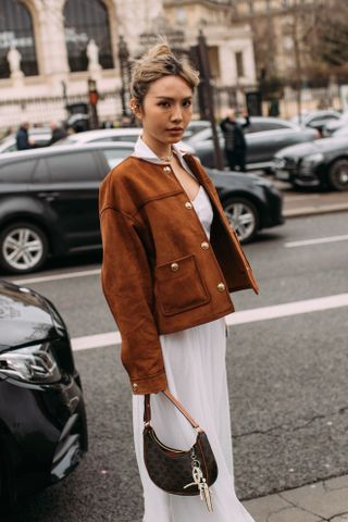 A woman at Paris Fashion Week wearing a suede brown collarless blazer and white dress