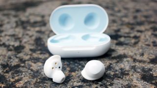 A close up of the rear side of one of the Samsung Galaxy Buds next to the charging case