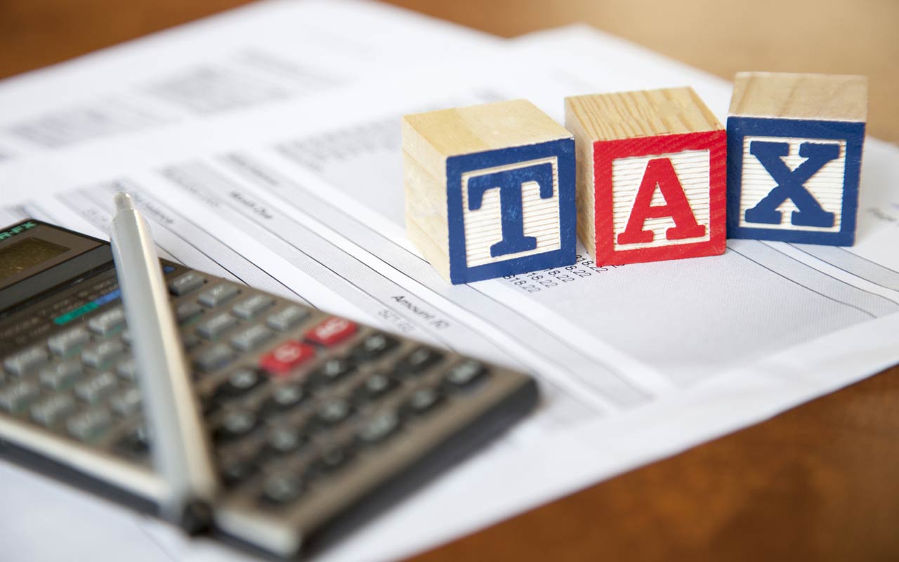 A calculator and blocks spelling out "tax" sitting atop of financial paperwork.