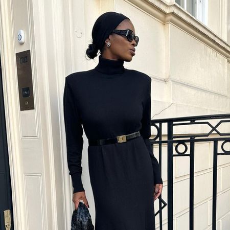 Woman wears black knit dress, black sunglasses and black belt