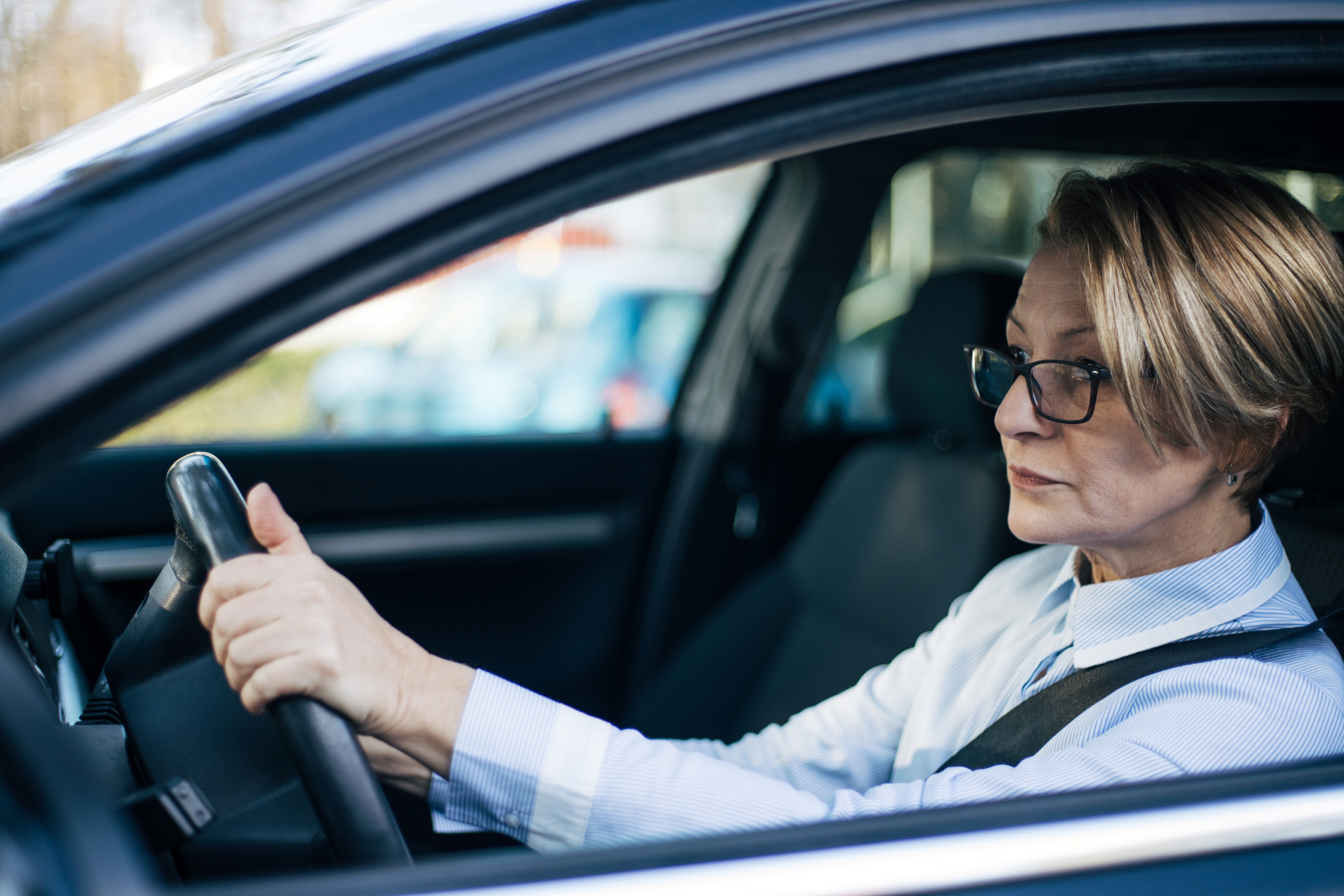 A middle aged woman drives a car through a neighborhood.