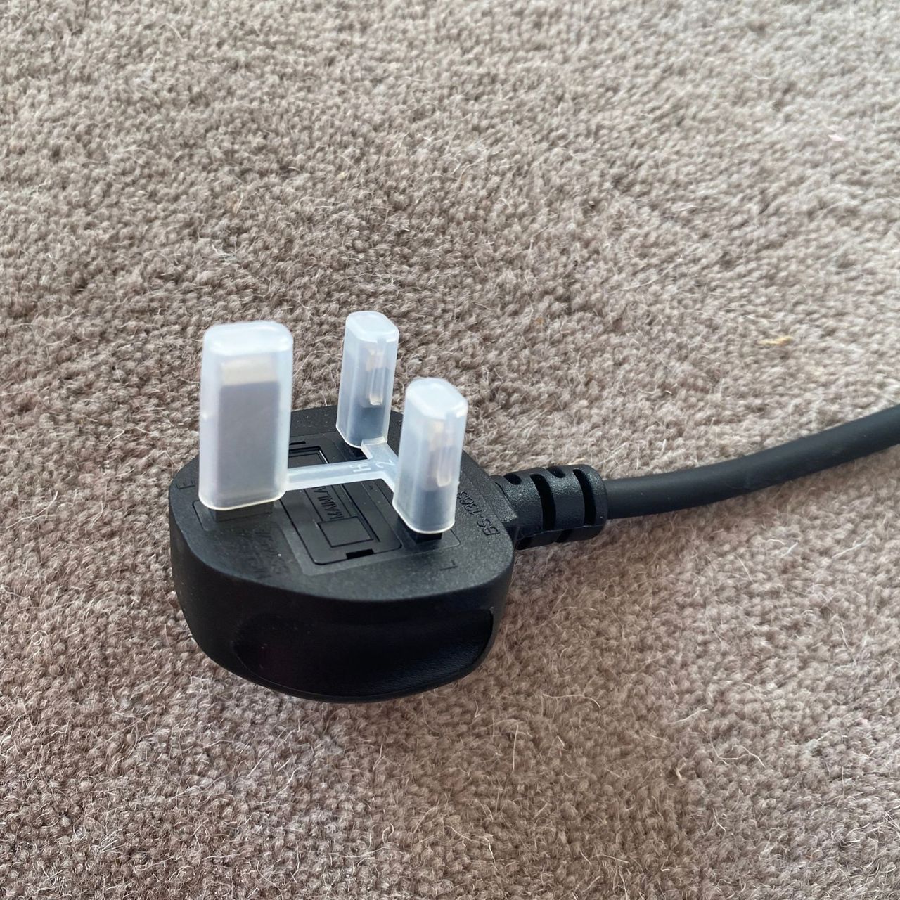 Plug of the Morphy Richards HeatFlux 1.5kW Ceramic Fan Heater with a plastic cap, on a neutral rug