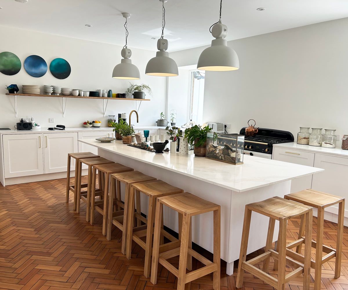 A white marble kitchen island with wooden chairs and overhead lighting