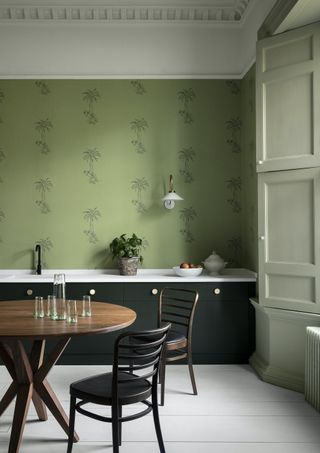 A kitchen with black cabinets and green wallpaper behind a wooden dining table with dark wooden chairs
