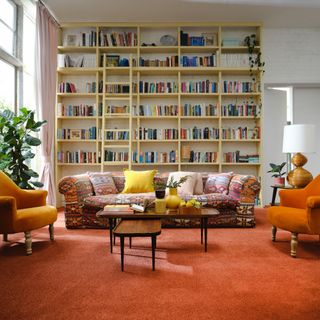 best carpet colour for living room, living room with orange carpet, large bookcase, orange armchairs, multicoloured sofa, wood coffee table nest