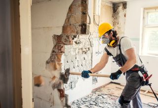 A builder swinging a sledgehammer and knocking down a blockwork internal wall