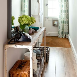 A narrow hallway with a slim console table storing hampers, baskets and boxes