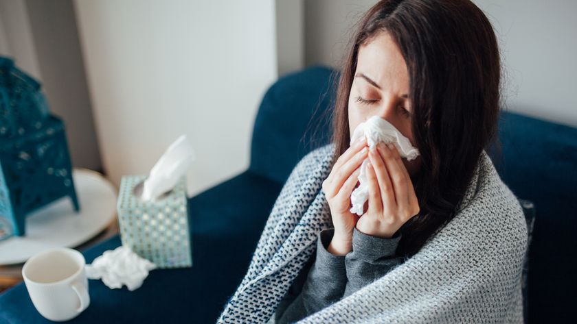 Sick woman blowing her nose while covered with a blanket.