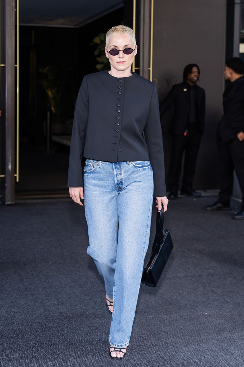 Jude Mack wearing a black collarless blazer, blue jeans, and sandals