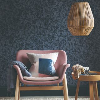 A living room with an abstract printed navy wallpaper and a pink chair with a colour-blocked cushion