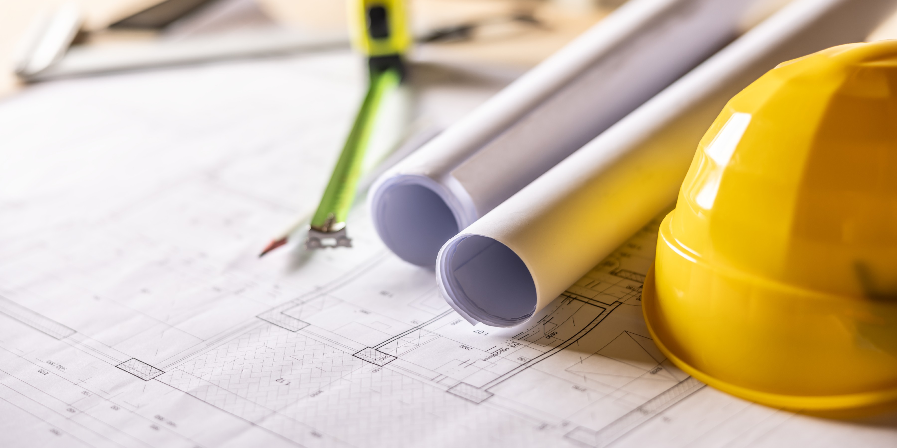 Extension plans, tape measure and yellow hard hat laid out on a table