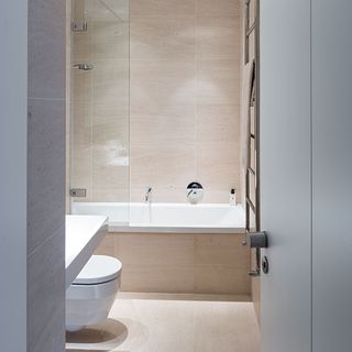 bathroom with cream colour tile wall bathtub commode and shelf