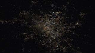 a city is seen at night from space by only its glowing lights on buildings and structures