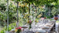 Alfresco garden dining table underneath vines. Table decorated with florals