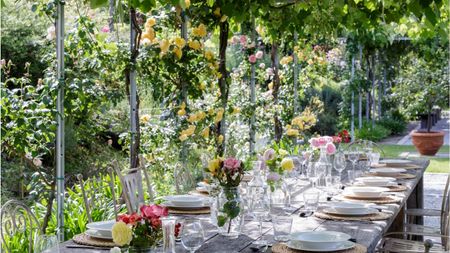 Alfresco garden dining table underneath vines. Table decorated with florals