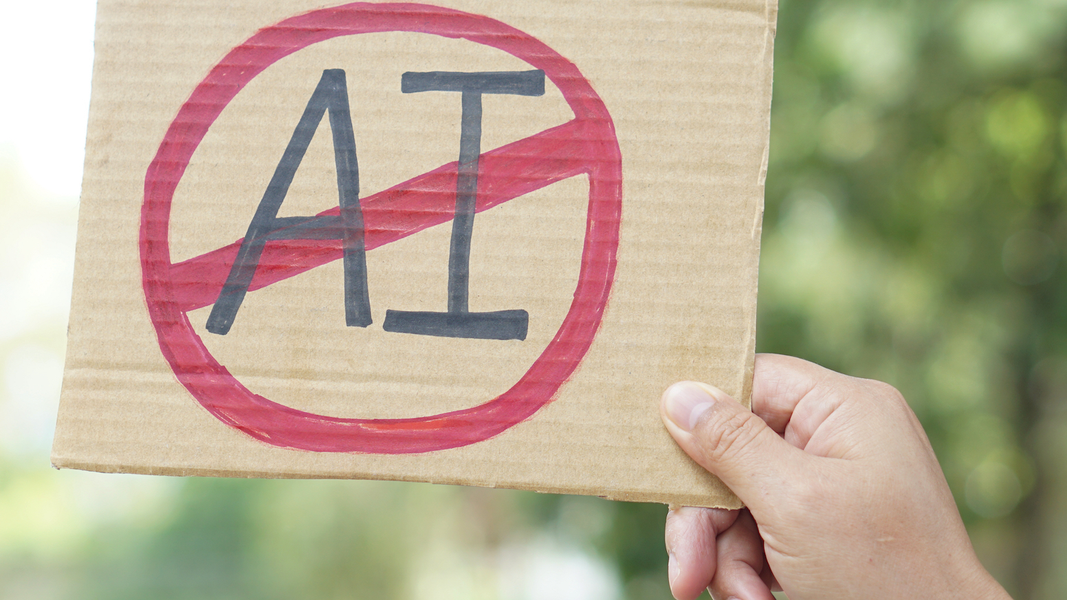 Close up hand holds paper card with No AI, prohibition sign