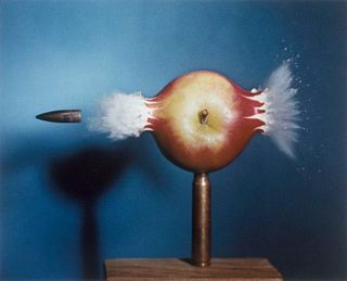 Motion shot of a bullet shooting through an apple against a dark blue background.