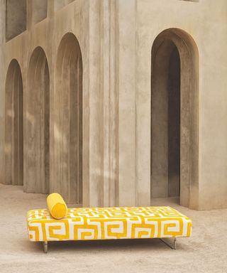 daybed in yellow patterned fabric outdoors against a stone wall