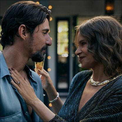 a man (Alberto Guerra as Dario) gazes at a woman (Sofia Vergara as Griselda) as she places a hand on his chest and holds a glass of champagne during a party