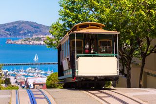 A cable car on a steep hill in San Francisco with the water in the background