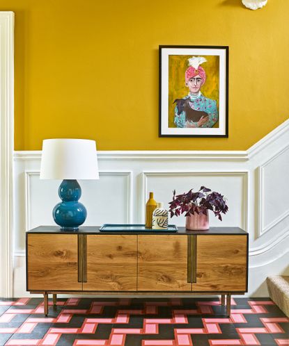 A modern hallway idea with yellow walls, white woodwork and a wooden mid-century modern sideboard