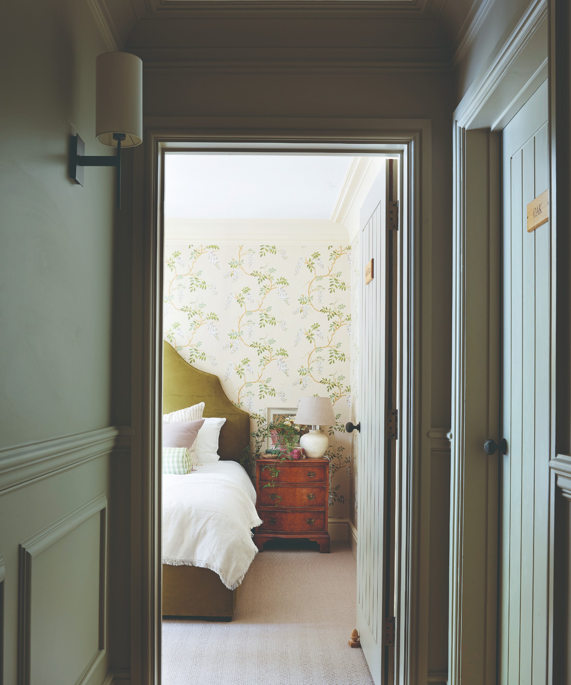 A hallway colour-drenched in olive green with a wall light and the door to the bedroom open