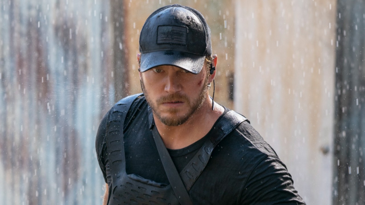 Chris Pratt looking mad and walking forward with a baseball hat on in the rain. 