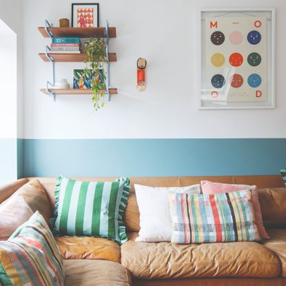 A living room with a corner brown leather sofa and a two-tone wall in blue and white