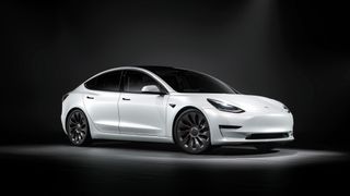 A white Telsa Model 3 in a studio with a black background