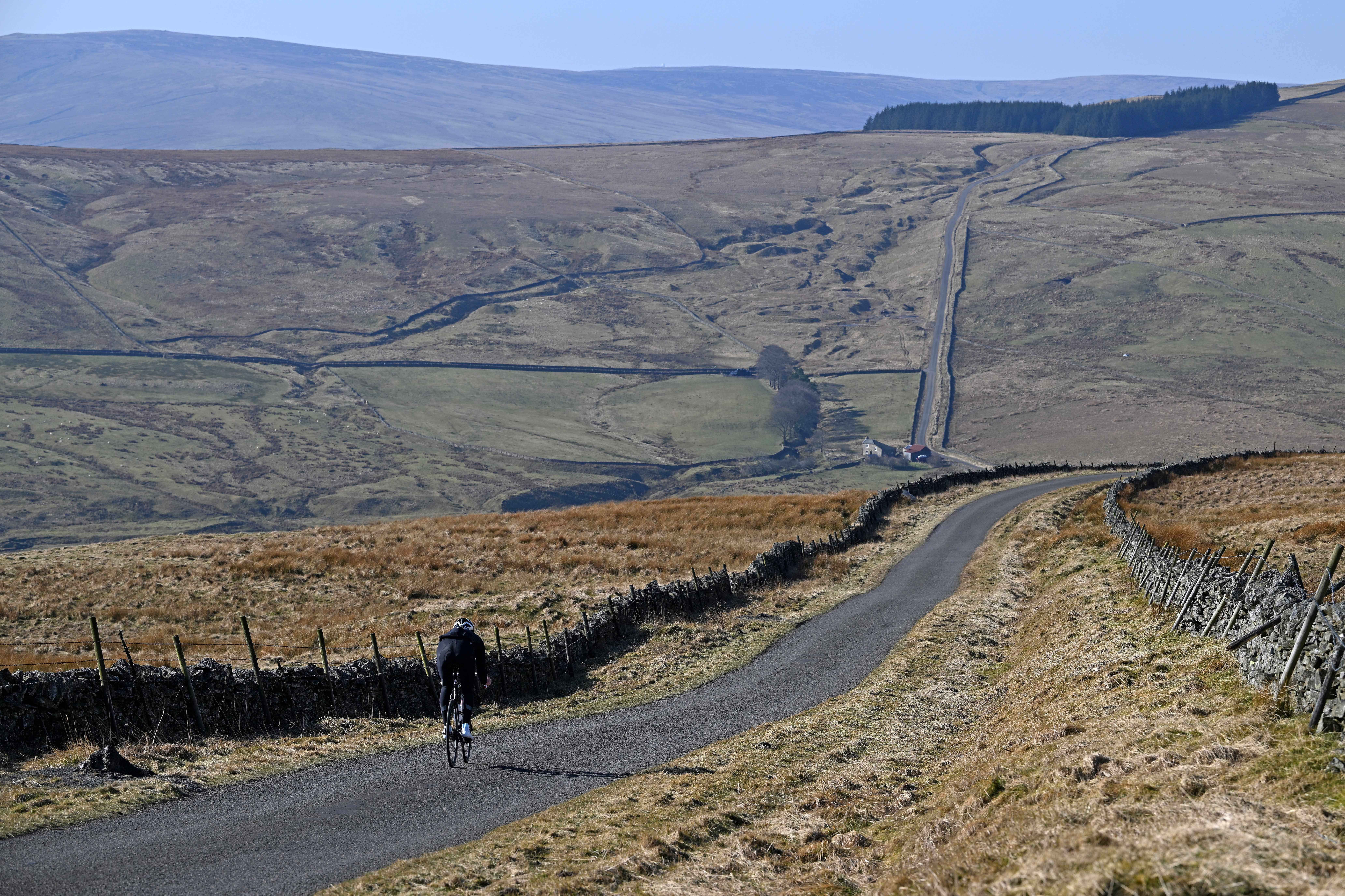 Man cycles along a road with hills in background