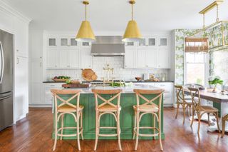 White kitchen with a green island, green patterned wallpaper and wooden bar stools