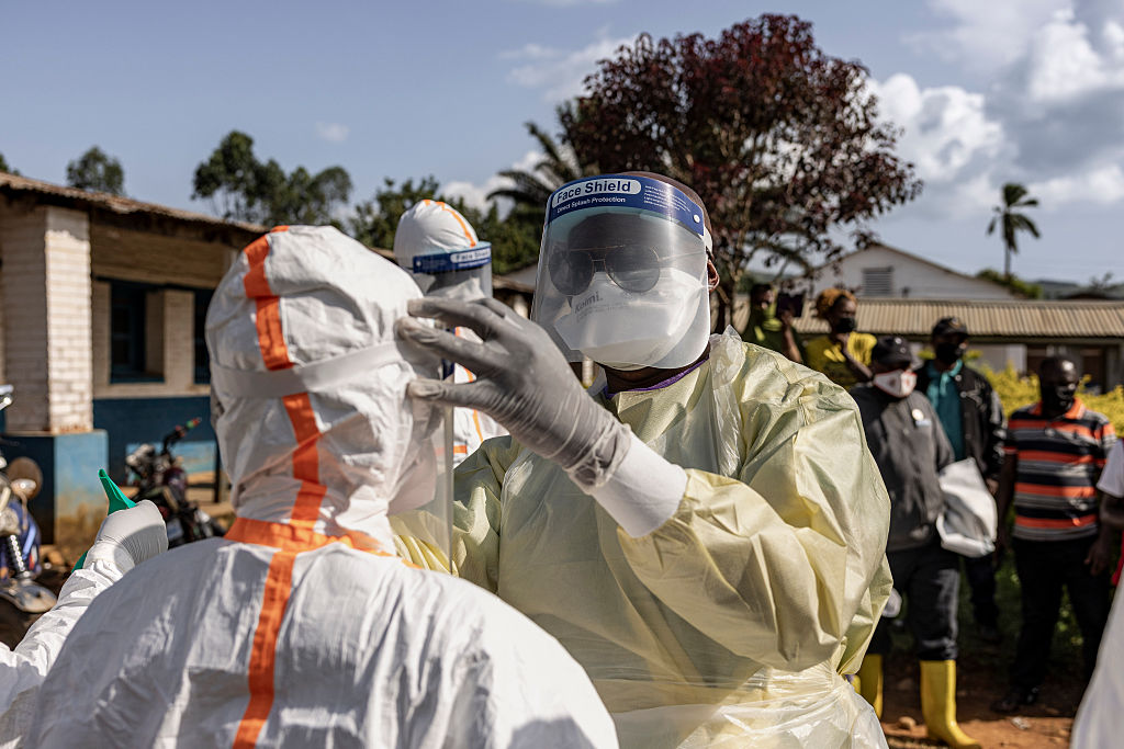 A person wearing a clean suit, mask and gloves tests another individual wearing another clean suit.