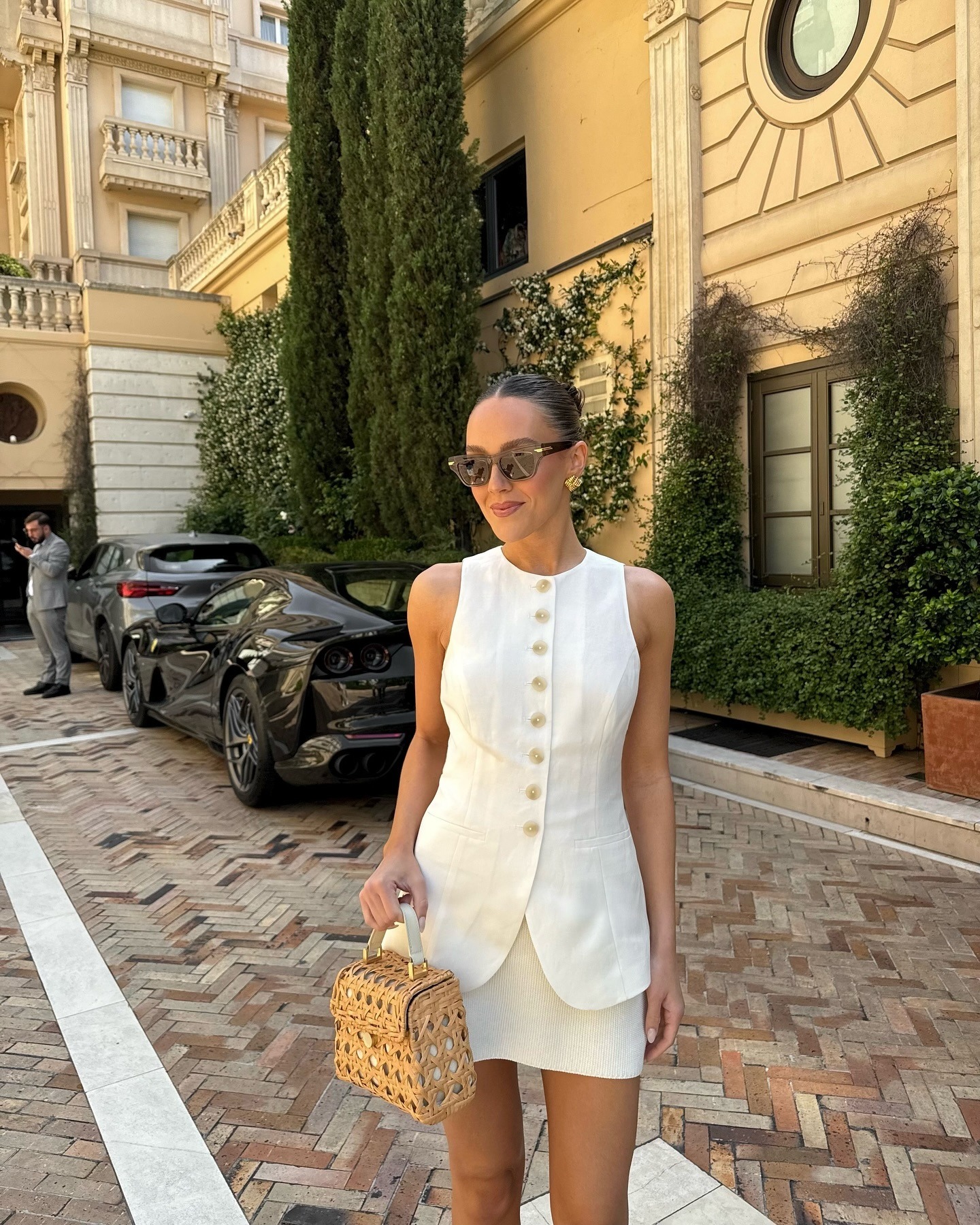 Influencer wearing white linen vest, linen mini skirt, and raffia bag while on European vacation.