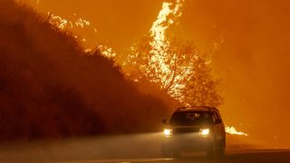 A car driving by a raging wildfire