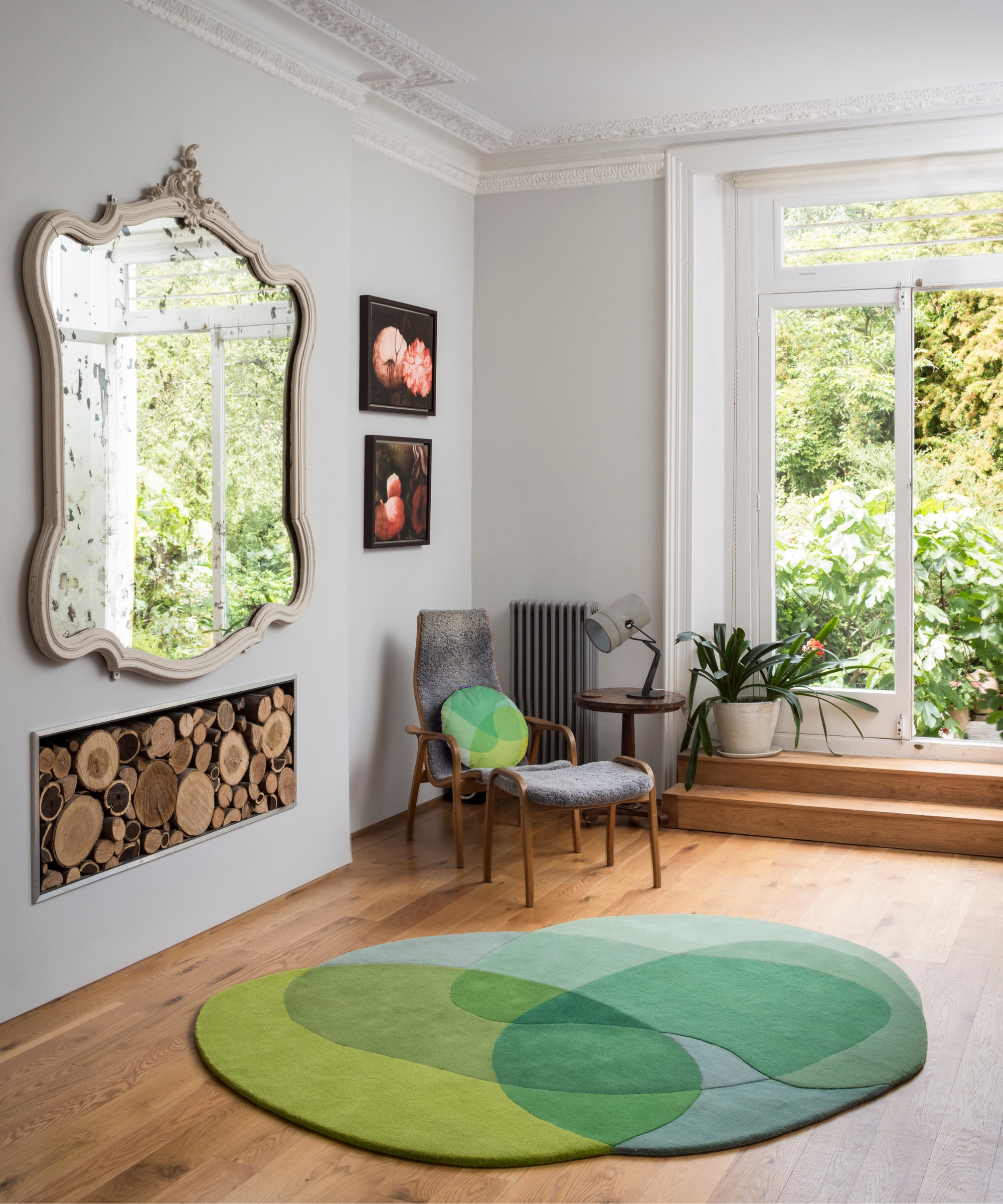 Round green abstract rug in bright room with ornate mirror, wooden armchair, and log store built-in.