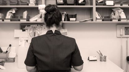 Sepia photograph of the back of a brunette lady wearing black with hair in a messy bun 