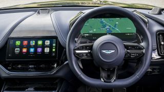 A car's steering wheel and dashboard showing Apple CarPlay Ultra
