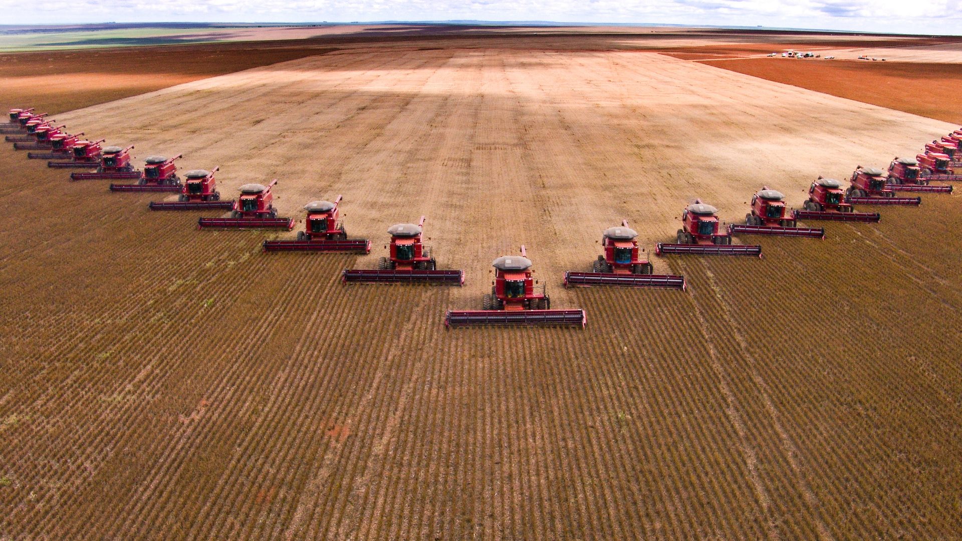 A row of tractors ride through dirt fields
