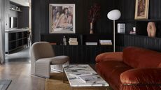 dark living room with orange velvet sofa, arm chair, marble coffee table, and floor lamp