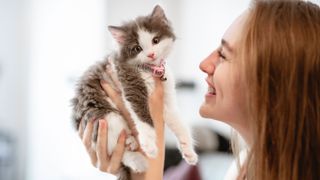 Woman holding up a kitten and smiling while it looks at the camera