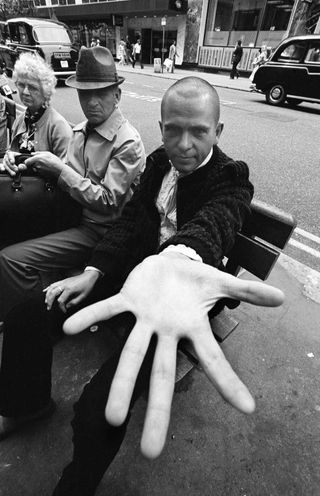 Posed portrait of Peter Gabriel sitting on a bench in the street