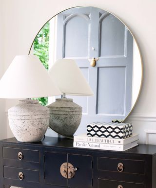 large circular mirror with large lamp and books on a side table