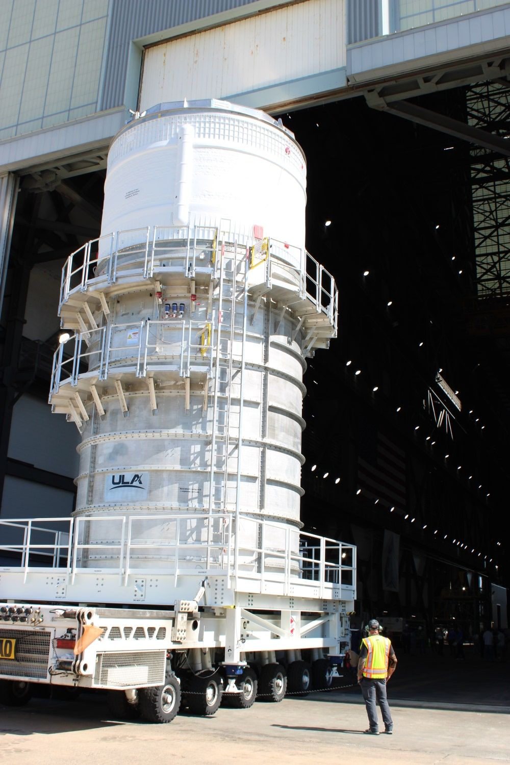 a large section of a rocket stands in the entrance of a factory warehouse like building.