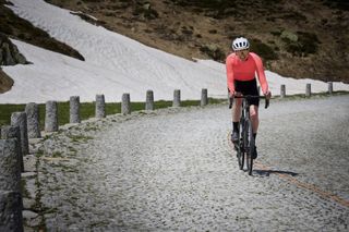 A male cyclist in a pink cycling jersey rides on the cobbles of the Gotthard Pass